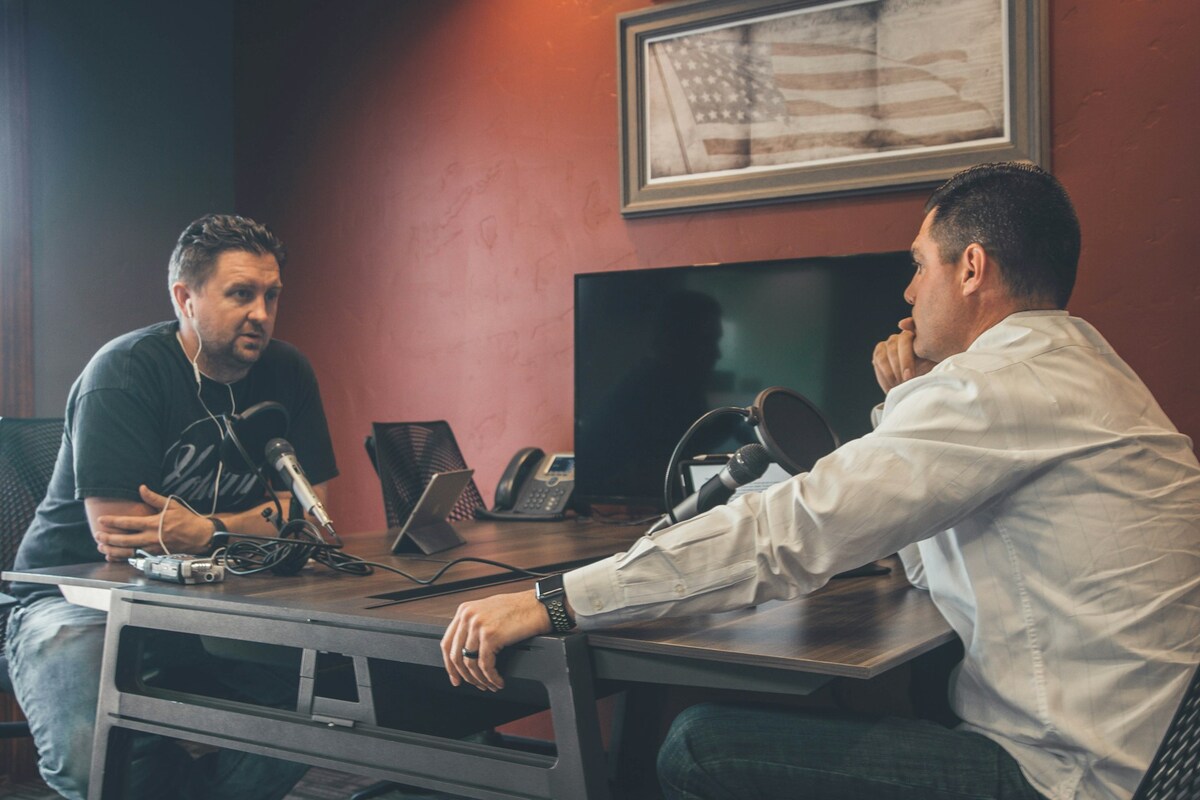 Man sitting in front of another man also sitting inside room for podcast