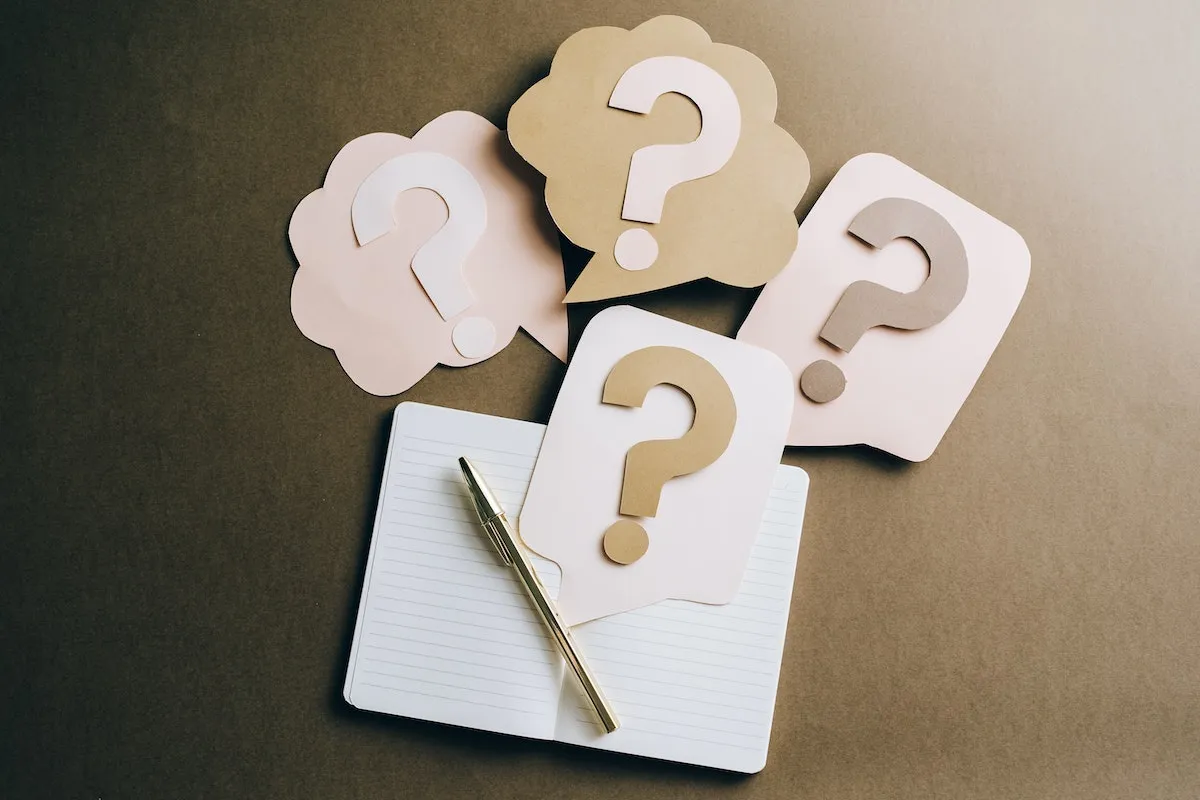 Paper question marks in speech bubbles above a notebook and pen