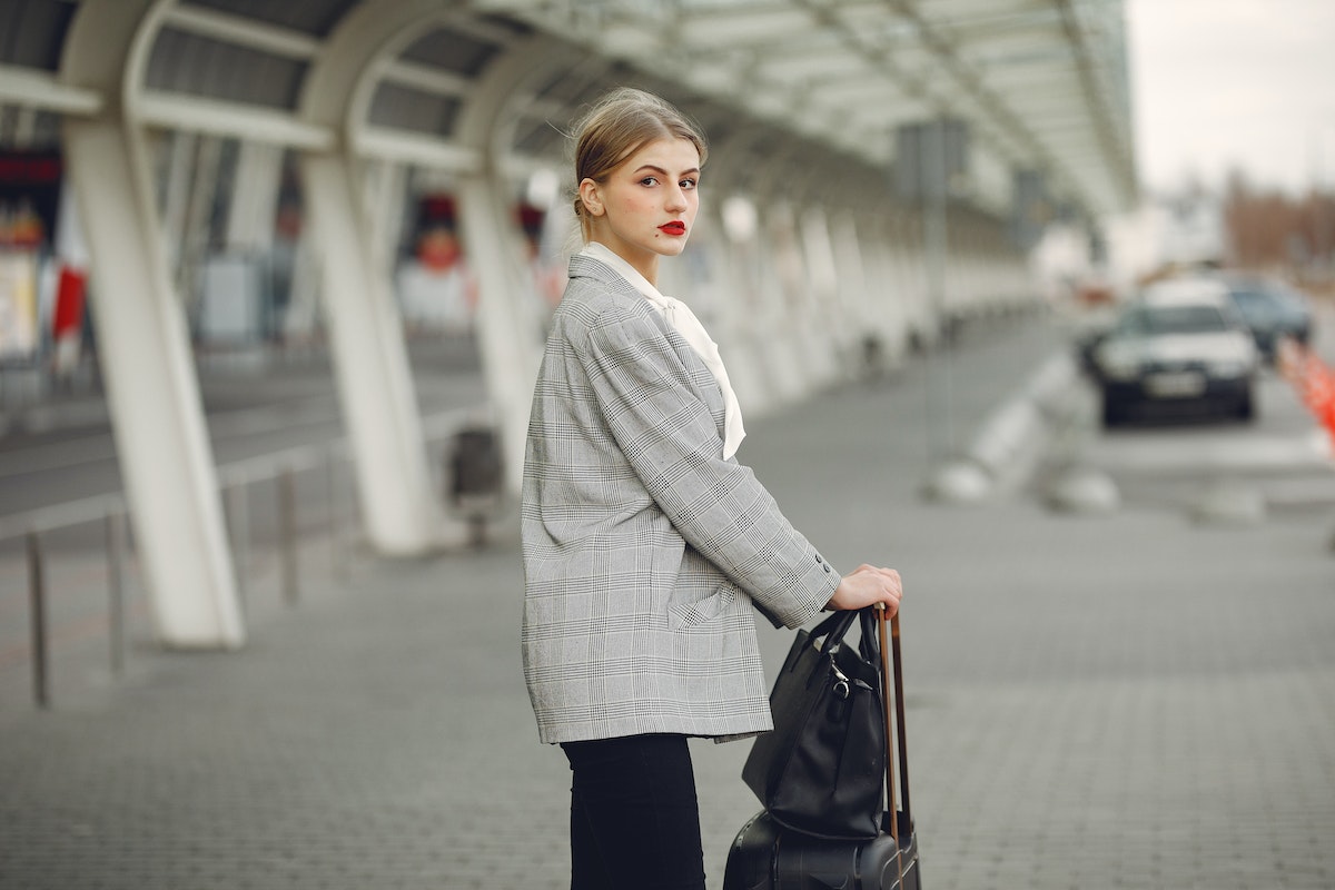 Stylish-young-woman-with-suitcase-near-car-parking-in-airport