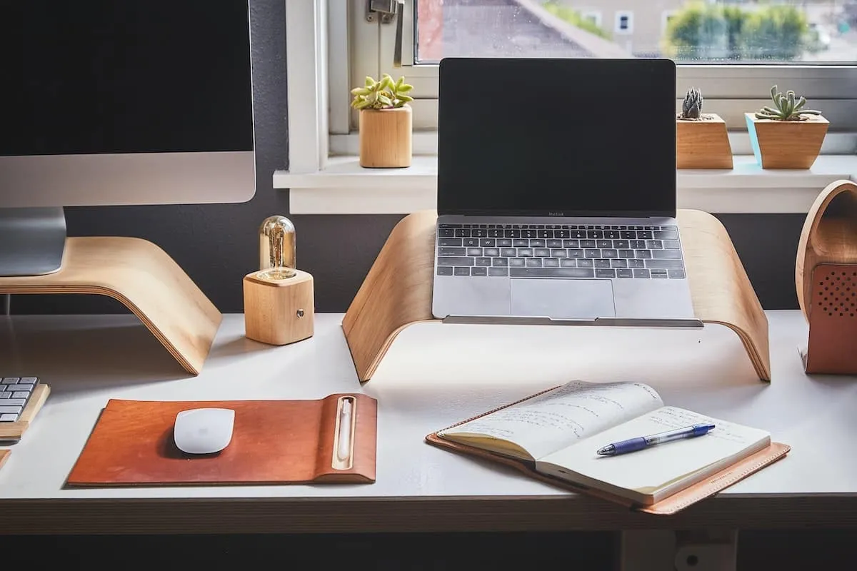 Laptop propped up on a desk with a notepad next to it.
