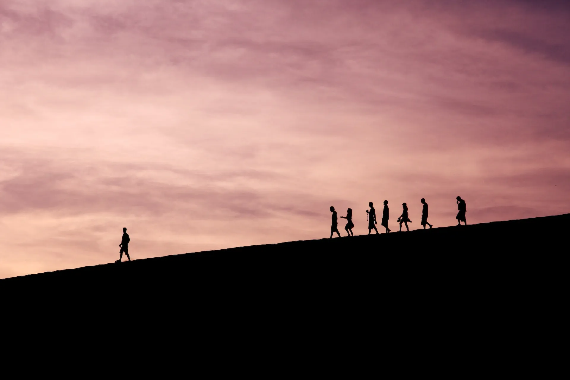 Silhouette of one person walking ahead of seven other people.