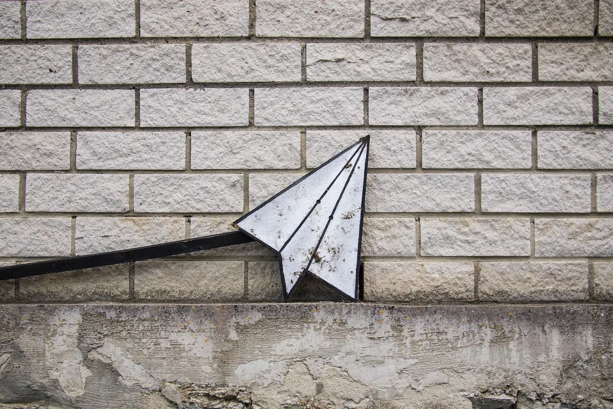 Image of a paper plane against a brick wall.