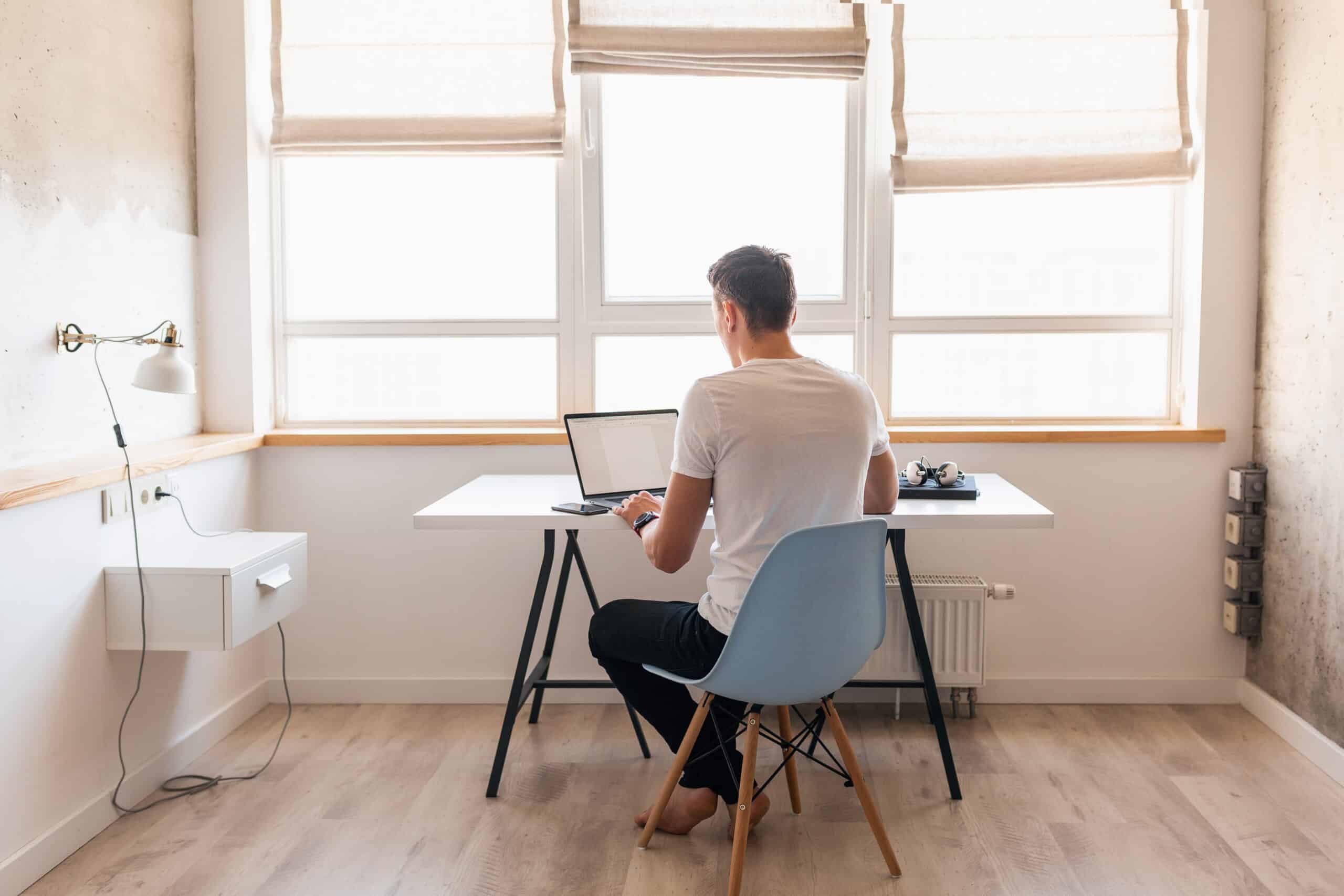 young man in casual outfit sitting at table working on laptop