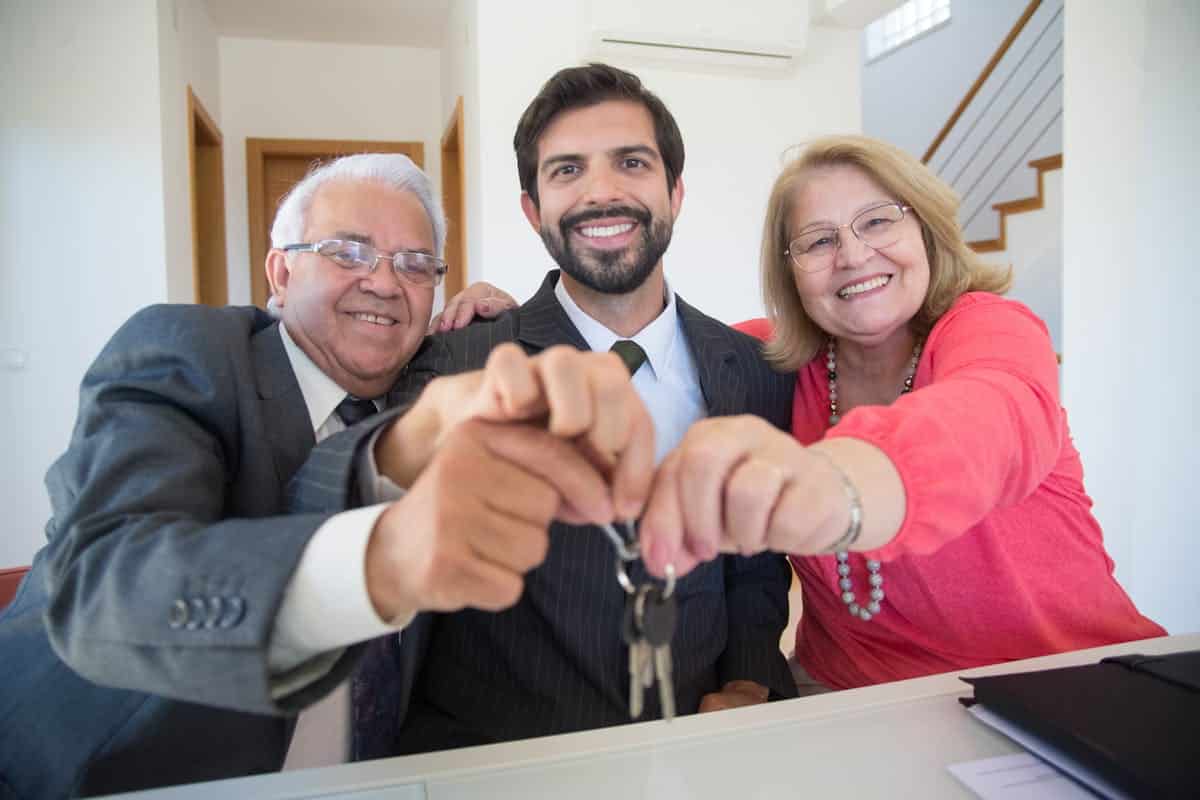 Elderly Couple Holding Keys of a House Besi8de a Man in Black Suit JacketElderly Couple Holding Keys of a House Besi8de a Man in Black Suit Jacket